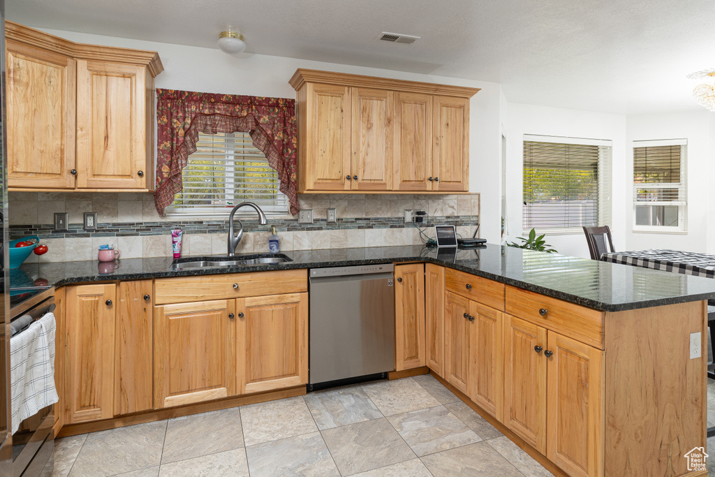 Kitchen featuring sink, a wealth of natural light, dark stone countertops, and stainless steel dishwasher