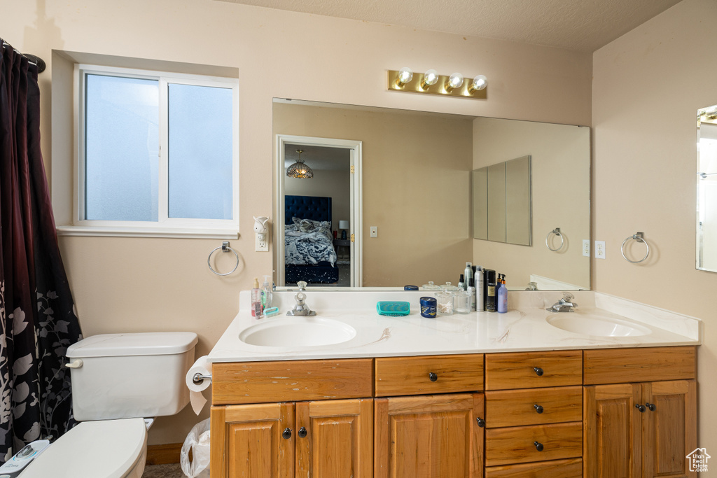 Bathroom with a healthy amount of sunlight, oversized vanity, double sink, and toilet