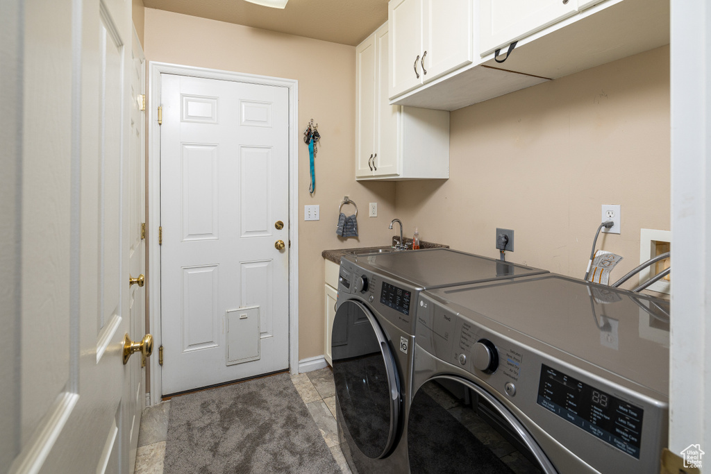 Clothes washing area featuring hookup for an electric dryer, light tile floors, sink, separate washer and dryer, and cabinets