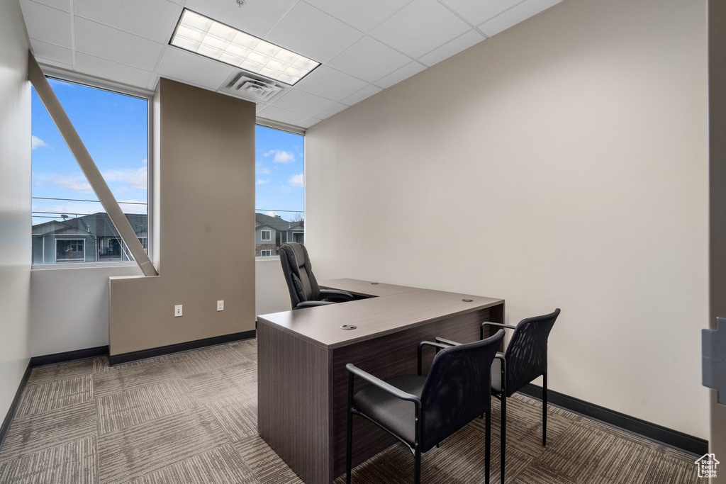 Office space with dark carpet, plenty of natural light, and a drop ceiling