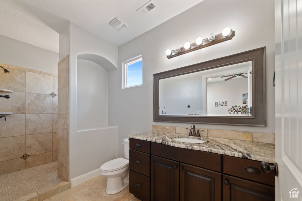 Bathroom with vanity, toilet, tile floors, a tile shower, and ceiling fan