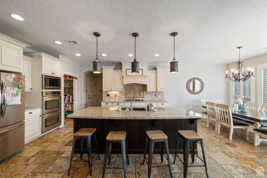 Kitchen with stainless steel appliances, light stone counters, a notable chandelier, and hanging light fixtures