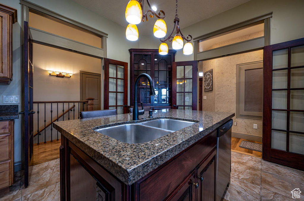 Kitchen with a notable chandelier, a kitchen island with sink, light tile floors, and pendant lighting