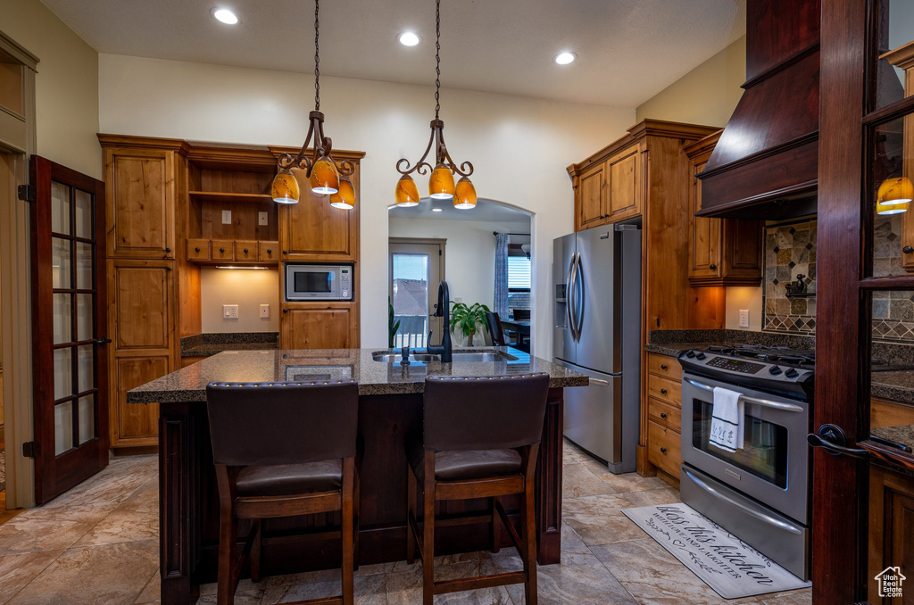 Kitchen with a kitchen island with sink, sink, a chandelier, dark stone counters, and stainless steel appliances