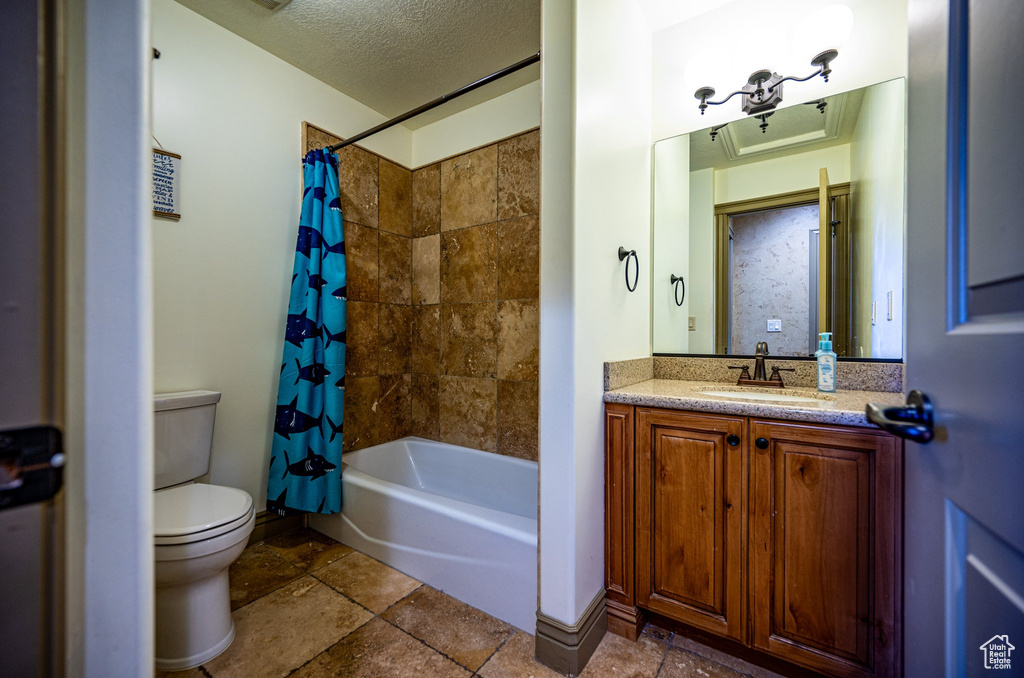 Full bathroom with a textured ceiling, shower / bathtub combination with curtain, tile flooring, vanity, and toilet