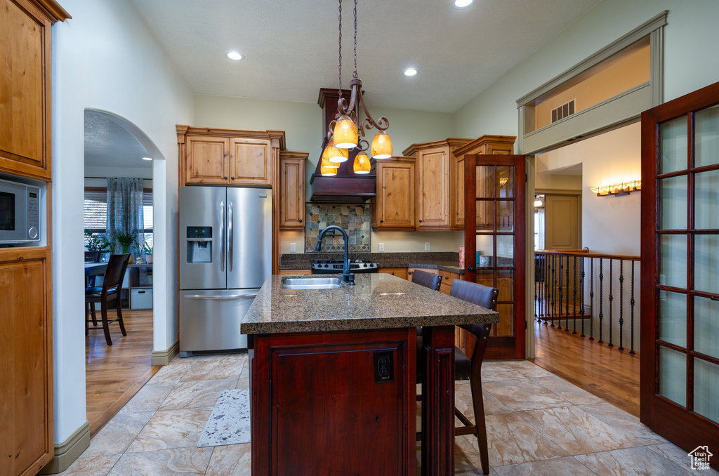 Kitchen featuring light tile flooring, a kitchen island with sink, pendant lighting, stainless steel refrigerator with ice dispenser, and an inviting chandelier
