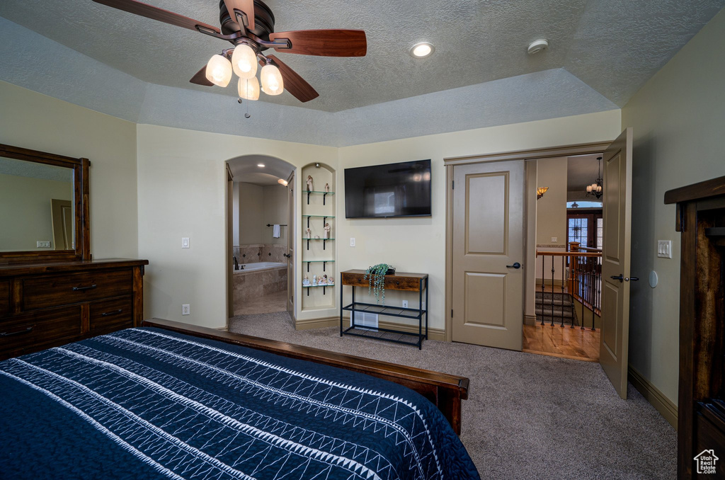 Bedroom featuring a raised ceiling, ensuite bathroom, a textured ceiling, dark colored carpet, and ceiling fan