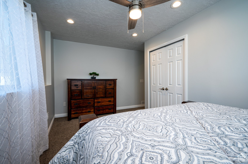 Bedroom with dark carpet, a textured ceiling, ceiling fan, and a closet