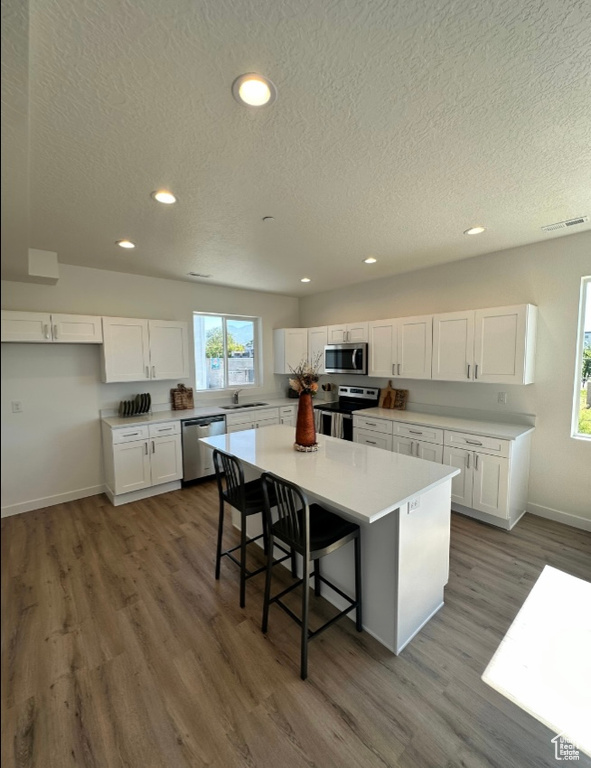 Kitchen featuring wood-type flooring, white cabinetry, a kitchen island, and stainless steel appliances