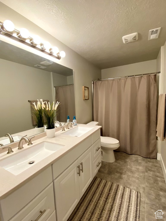 Bathroom with dual sinks, tile floors, a textured ceiling, large vanity, and toilet