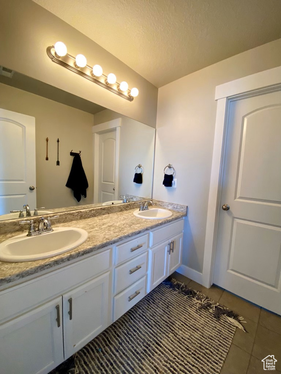 Bathroom with a textured ceiling, double sink vanity, and tile floors