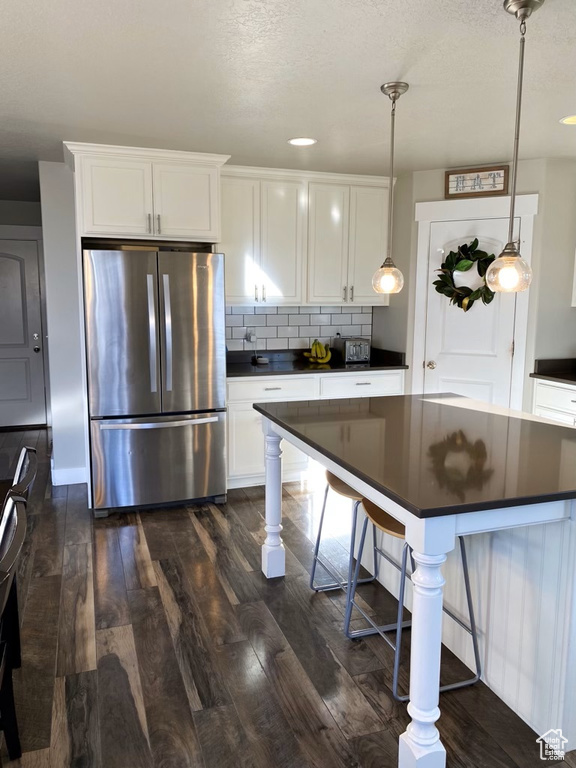 Kitchen featuring tasteful backsplash, stainless steel refrigerator, dark hardwood / wood-style floors, hanging light fixtures, and white cabinets