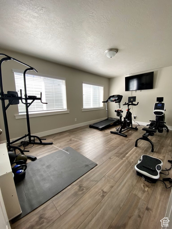 Workout room with light wood-type flooring and a textured ceiling