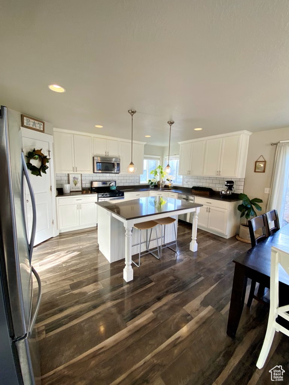 Kitchen with a kitchen island, dark wood-type flooring, appliances with stainless steel finishes, white cabinetry, and pendant lighting