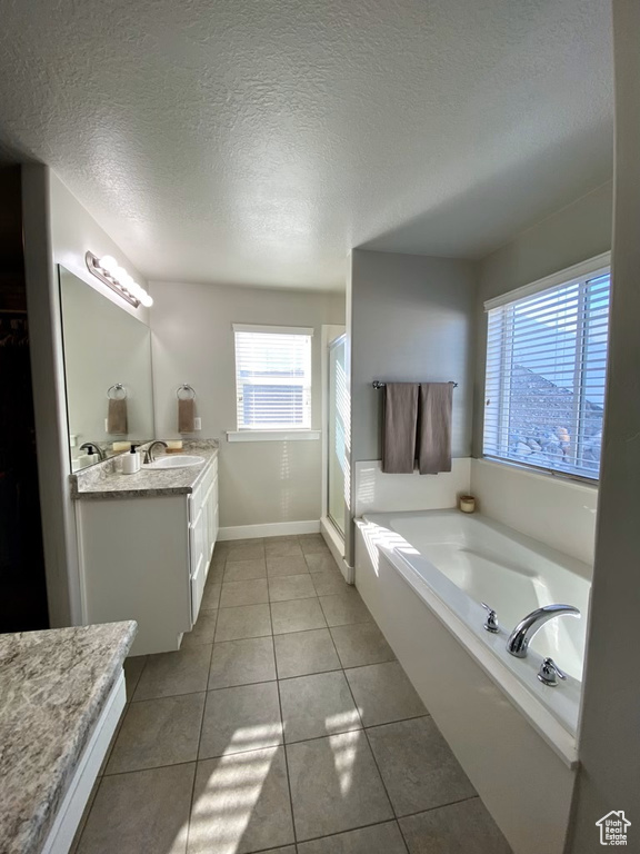 Bathroom featuring shower with separate bathtub, a textured ceiling, vanity with extensive cabinet space, and tile floors