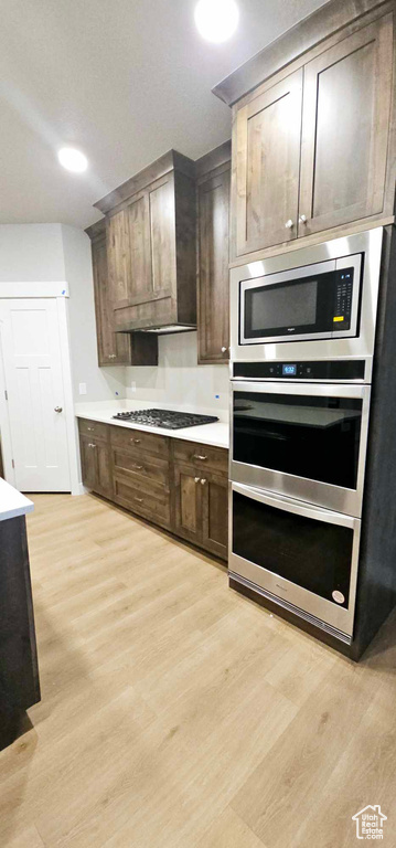 Kitchen with dark brown cabinets, light hardwood / wood-style flooring, stainless steel appliances, and custom range hood