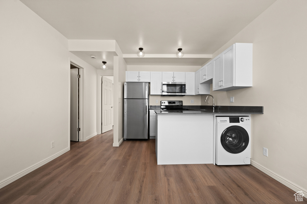 Kitchen with appliances with stainless steel finishes, washer / clothes dryer, white cabinetry, and dark hardwood / wood-style flooring