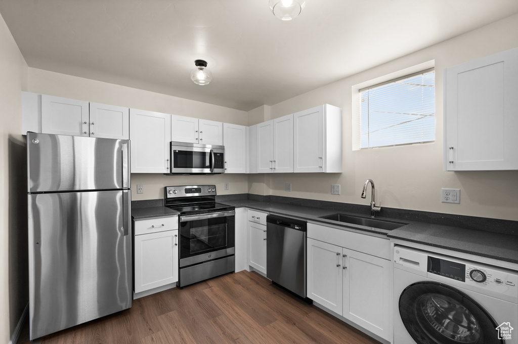 Kitchen featuring dark wood-type flooring, sink, white cabinets, washer / dryer, and stainless steel appliances
