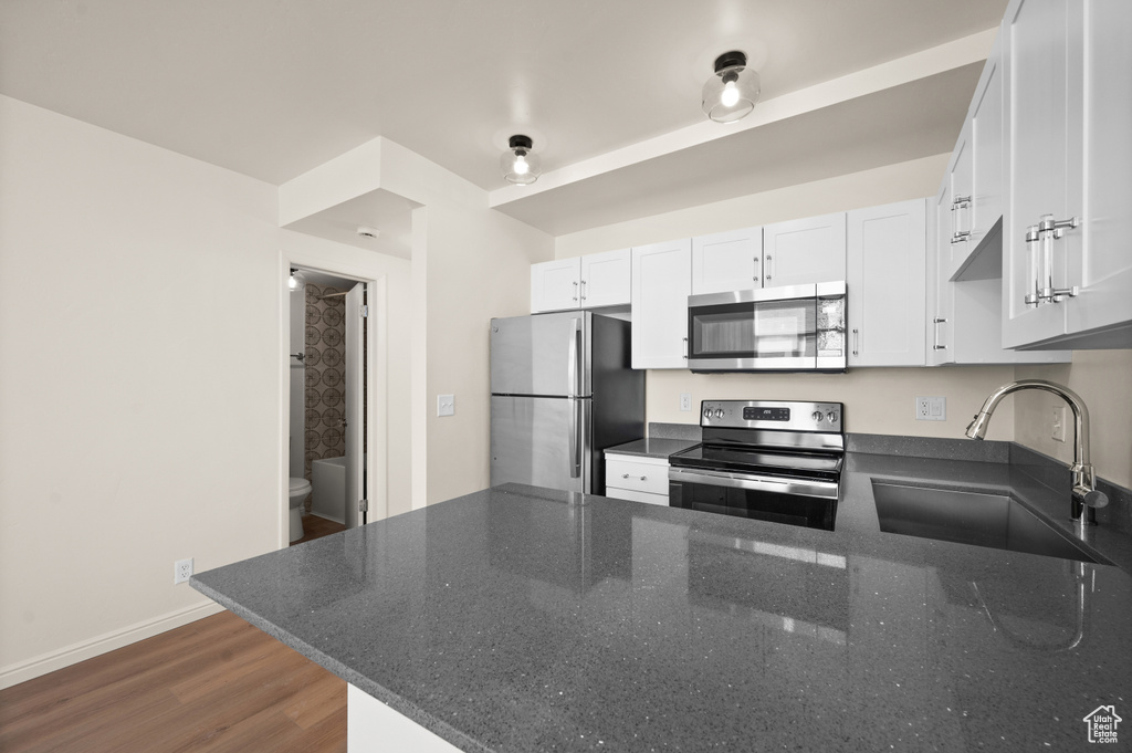 Kitchen featuring sink, dark wood-type flooring, kitchen peninsula, stainless steel appliances, and dark stone counters