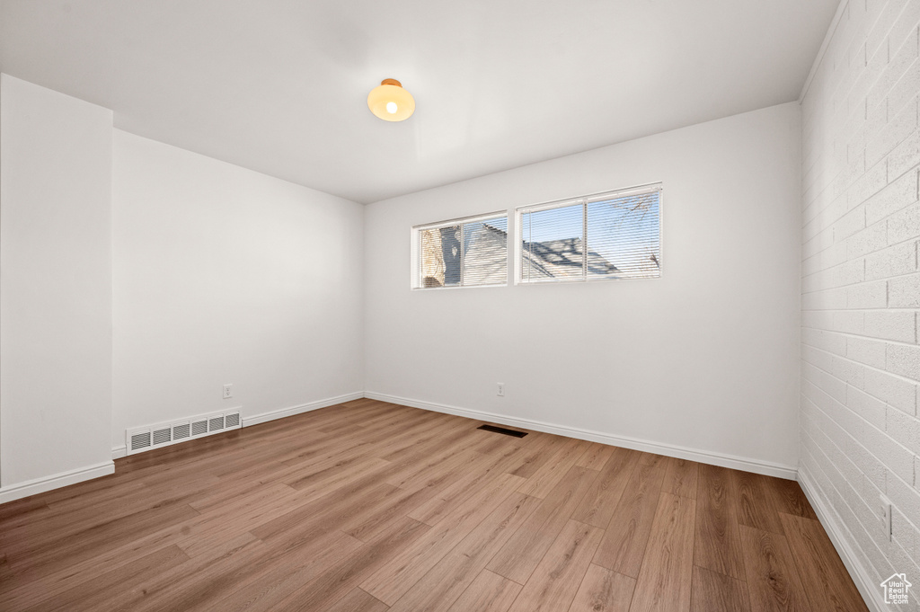 Spare room with brick wall and light hardwood / wood-style floors