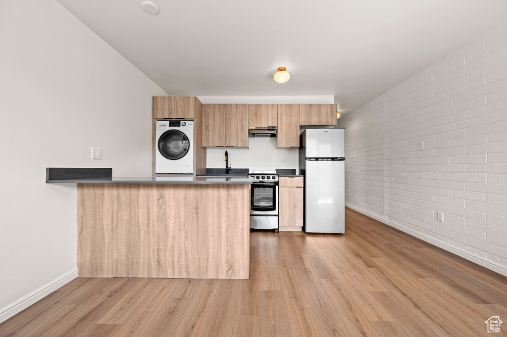 Kitchen with washer / dryer, brick wall, light hardwood / wood-style flooring, stainless steel electric range oven, and white refrigerator