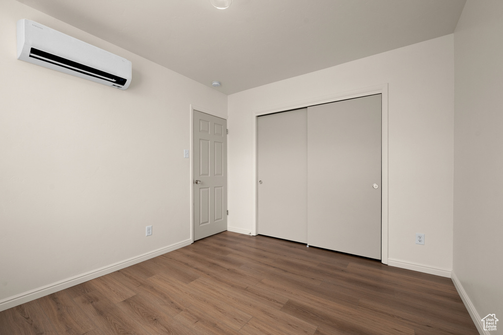 Unfurnished bedroom with dark wood-type flooring, a wall unit AC, and a closet