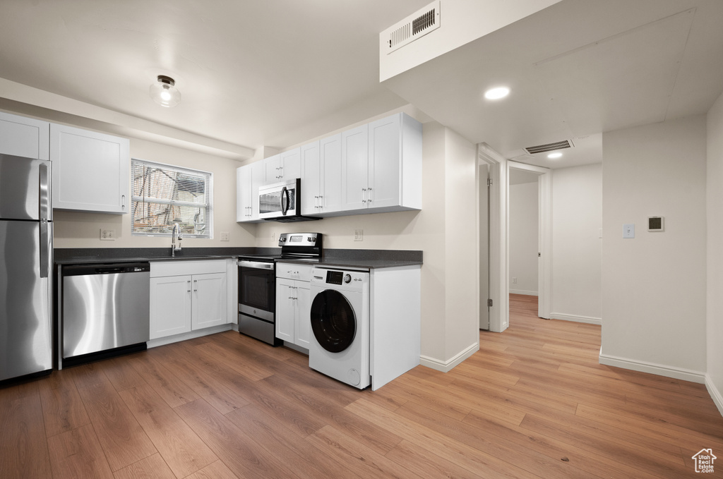 Kitchen featuring sink, appliances with stainless steel finishes, washer / clothes dryer, light hardwood / wood-style flooring, and white cabinets