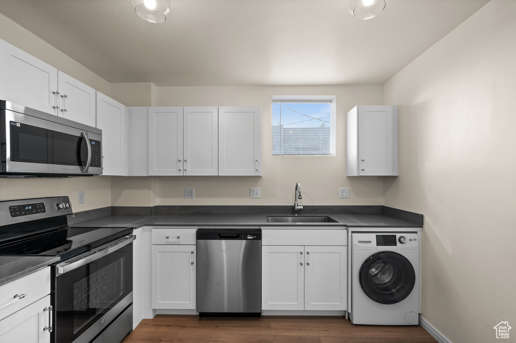 Kitchen with washer / dryer, appliances with stainless steel finishes, white cabinets, dark wood-type flooring, and sink