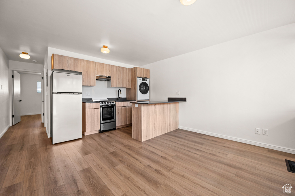 Kitchen featuring kitchen peninsula, white fridge, wood-type flooring, and stainless steel range oven