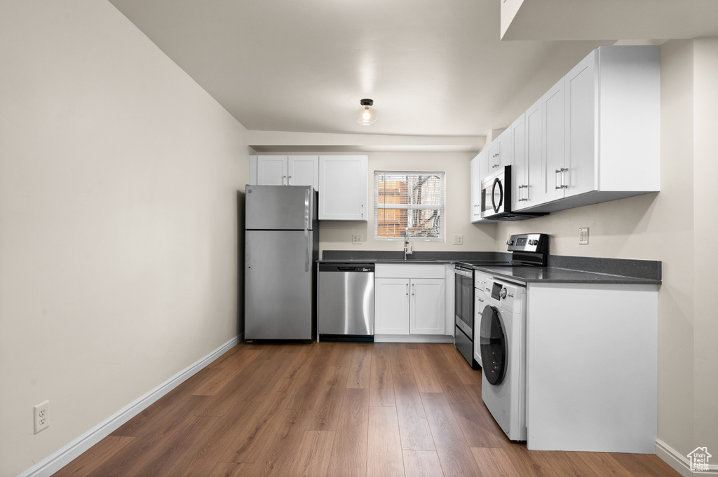 Kitchen featuring sink, white cabinets, wood-type flooring, washer / dryer, and stainless steel appliances