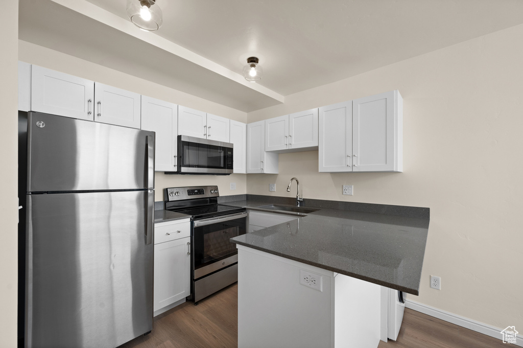 Kitchen with appliances with stainless steel finishes, white cabinets, sink, and dark wood-type flooring