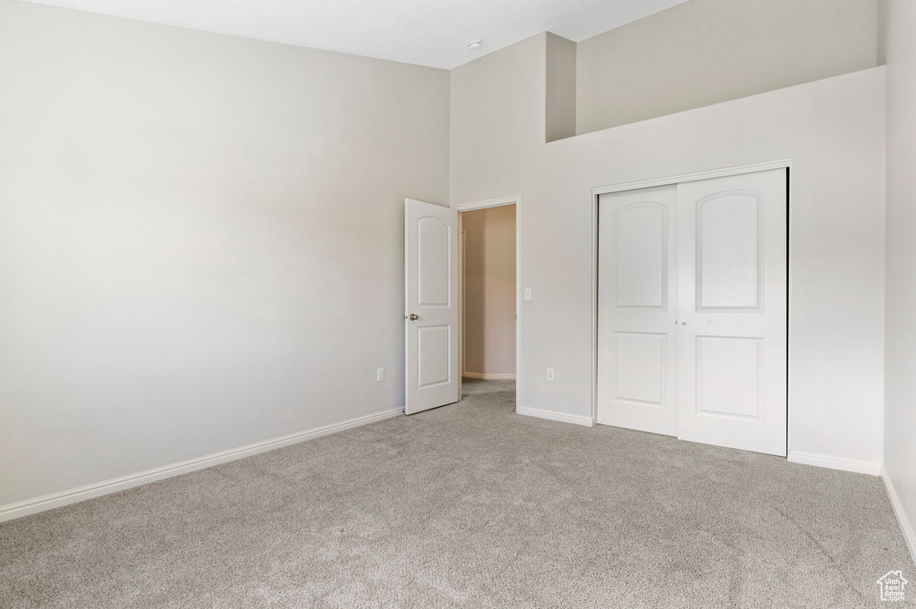 Unfurnished bedroom with light carpet, a closet, and a high ceiling