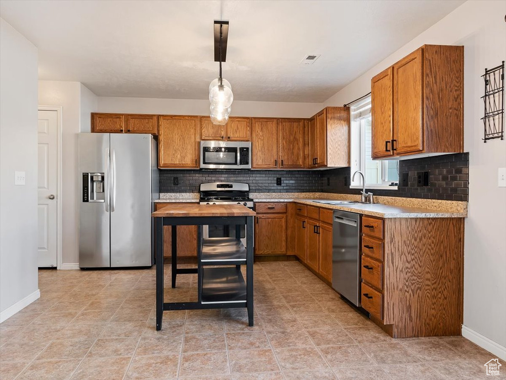 Kitchen with appliances with stainless steel finishes, light tile floors, sink, and backsplash