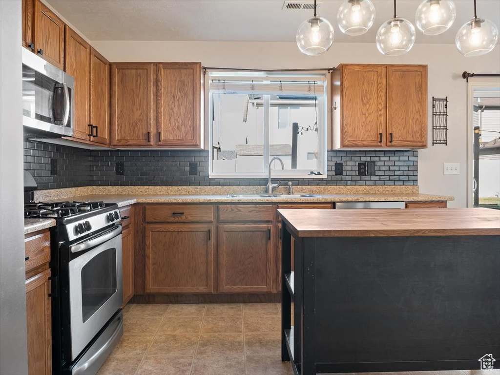 Kitchen featuring appliances with stainless steel finishes, pendant lighting, tasteful backsplash, and butcher block countertops