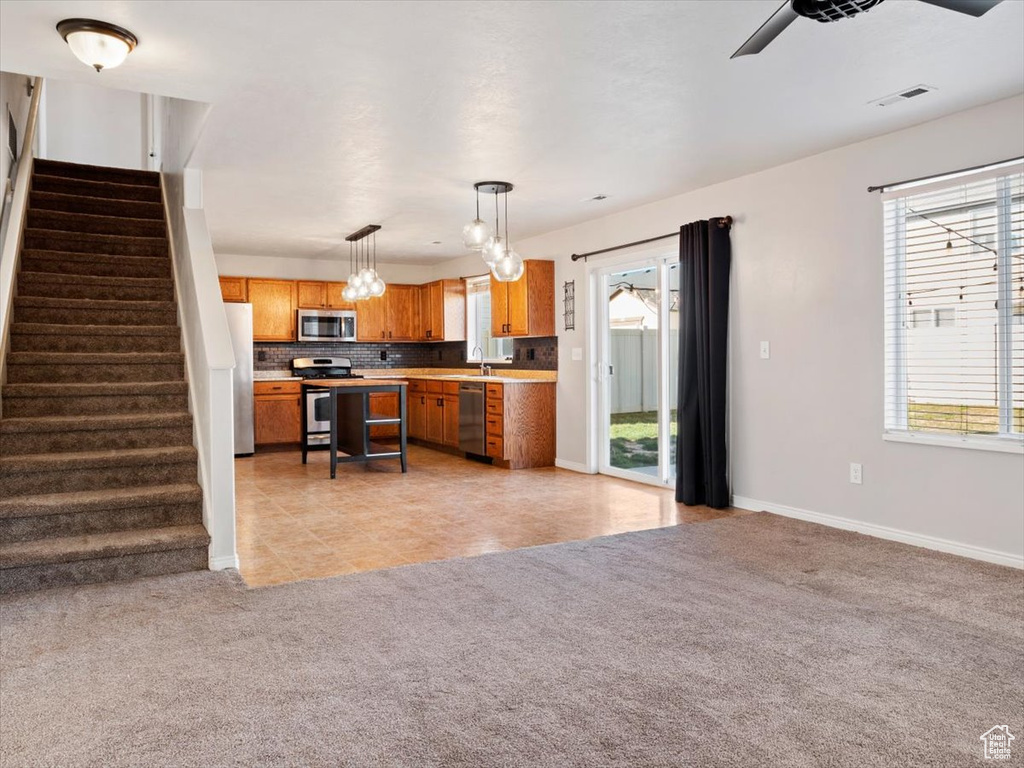 Kitchen with decorative light fixtures, plenty of natural light, ceiling fan with notable chandelier, and light carpet