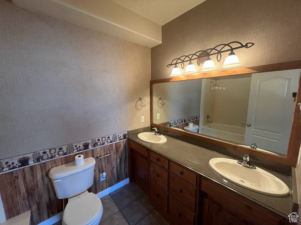 Bathroom featuring vanity with extensive cabinet space, tile floors, dual sinks, and toilet