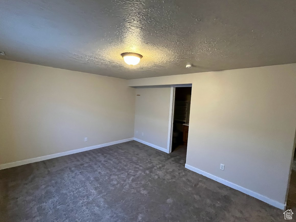 Unfurnished bedroom featuring dark carpet, a textured ceiling, and a closet
