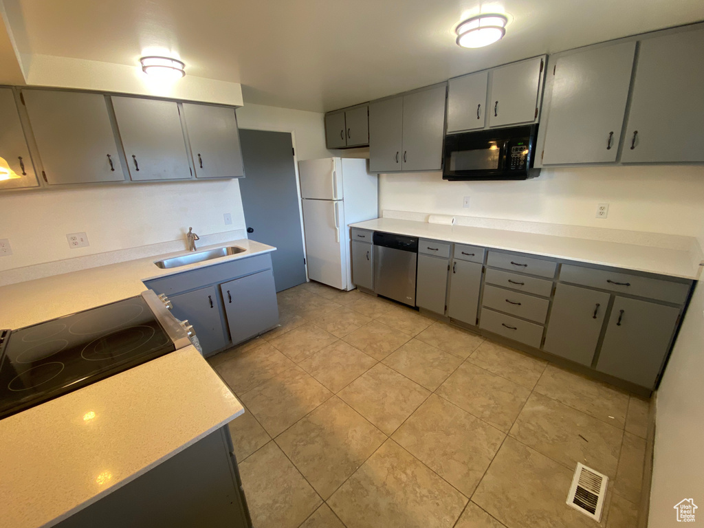 Kitchen featuring sink, white fridge, stainless steel dishwasher, gray cabinetry, and light tile floors