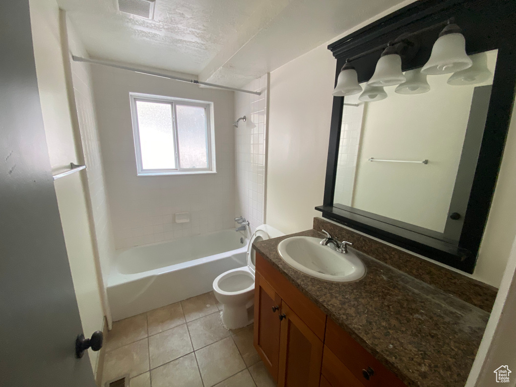 Full bathroom with a textured ceiling, tile floors, vanity, toilet, and tiled shower / bath combo
