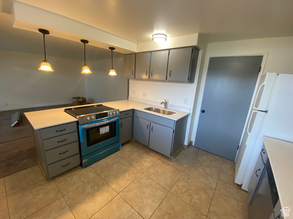 Kitchen featuring sink, white fridge, stainless steel electric range oven, kitchen peninsula, and decorative light fixtures