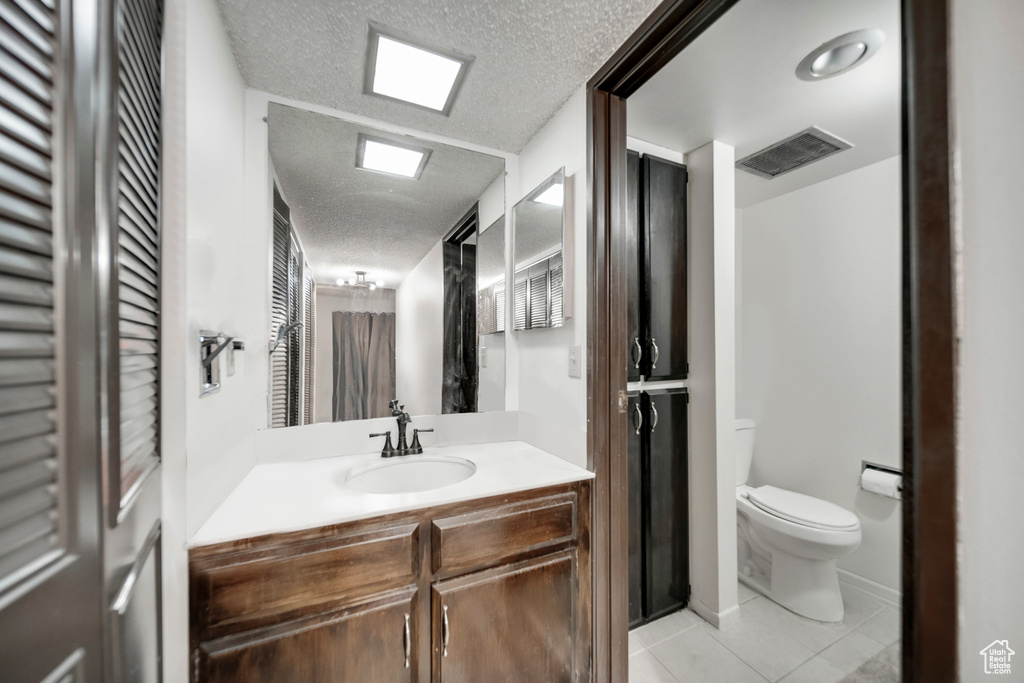 Bathroom with tile flooring, vanity with extensive cabinet space, a textured ceiling, and toilet