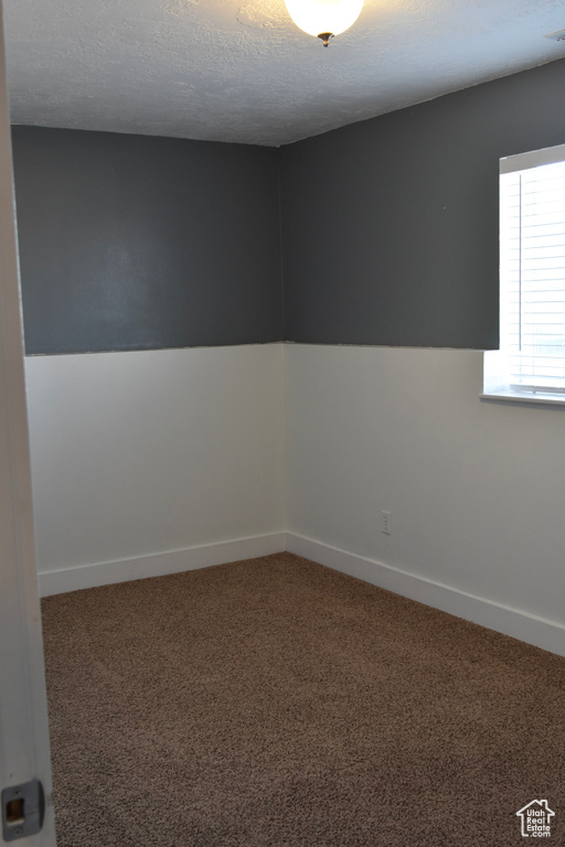 Unfurnished room featuring a textured ceiling and dark colored carpet