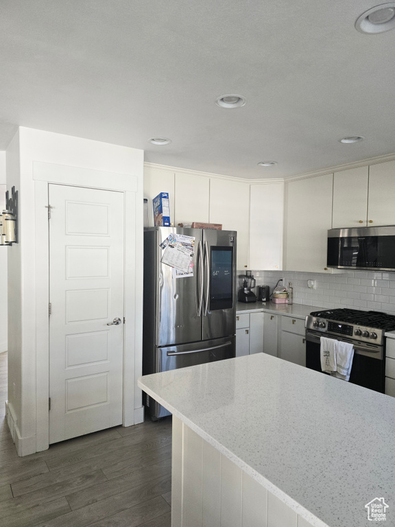 Kitchen with white cabinets, stainless steel appliances, backsplash, light stone countertops, and dark hardwood / wood-style flooring