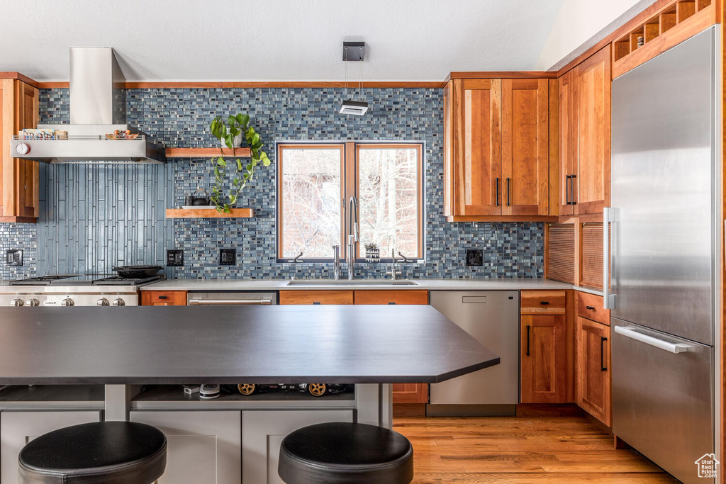 Kitchen featuring sink, wall chimney range hood, backsplash, light hardwood / wood-style flooring, and stainless steel appliances