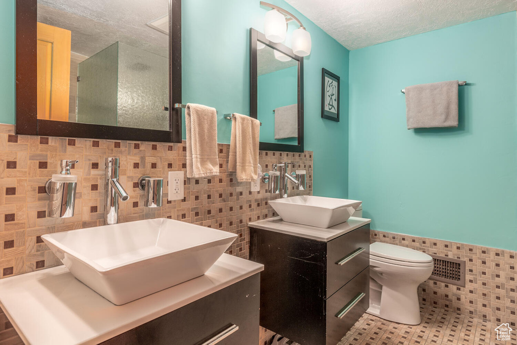 Bathroom featuring vanity with extensive cabinet space, backsplash, tile walls, and toilet