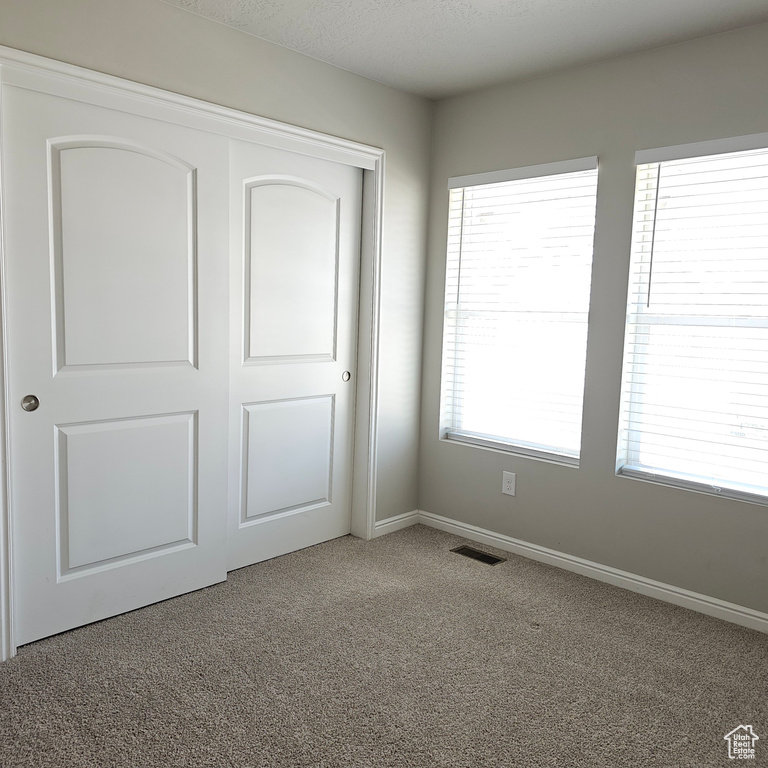 Unfurnished bedroom with light colored carpet, multiple windows, and a closet