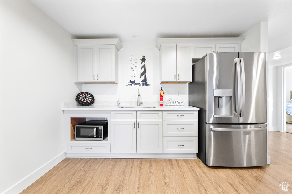 Kitchen featuring stainless steel appliances, white cabinets, sink, and light wood-type flooring