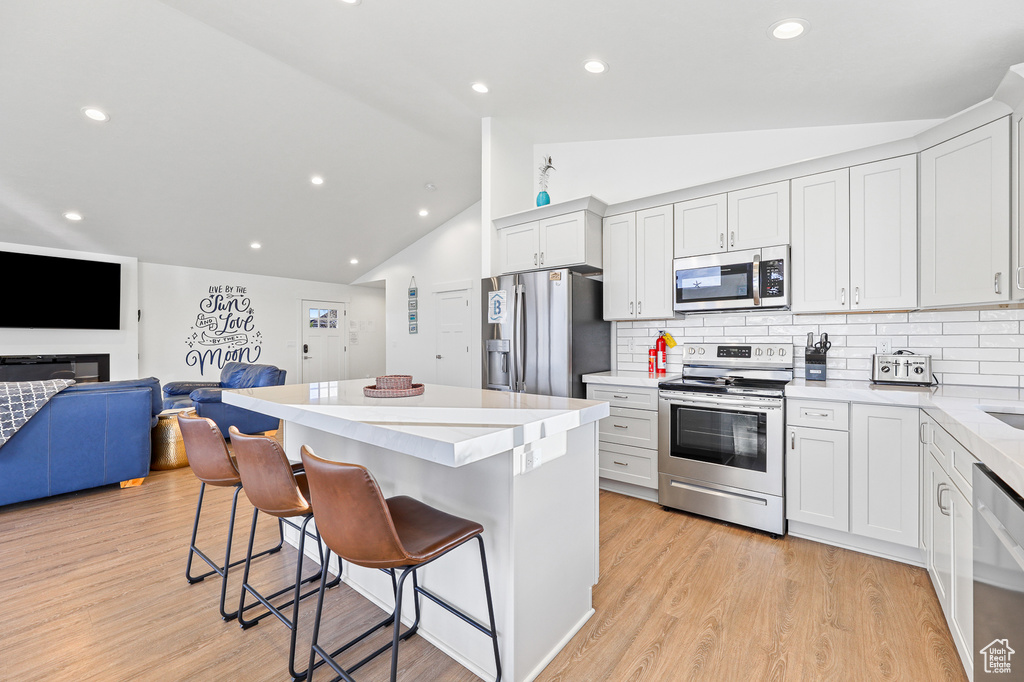 Kitchen with appliances with stainless steel finishes, a kitchen island, light hardwood / wood-style floors, lofted ceiling, and tasteful backsplash