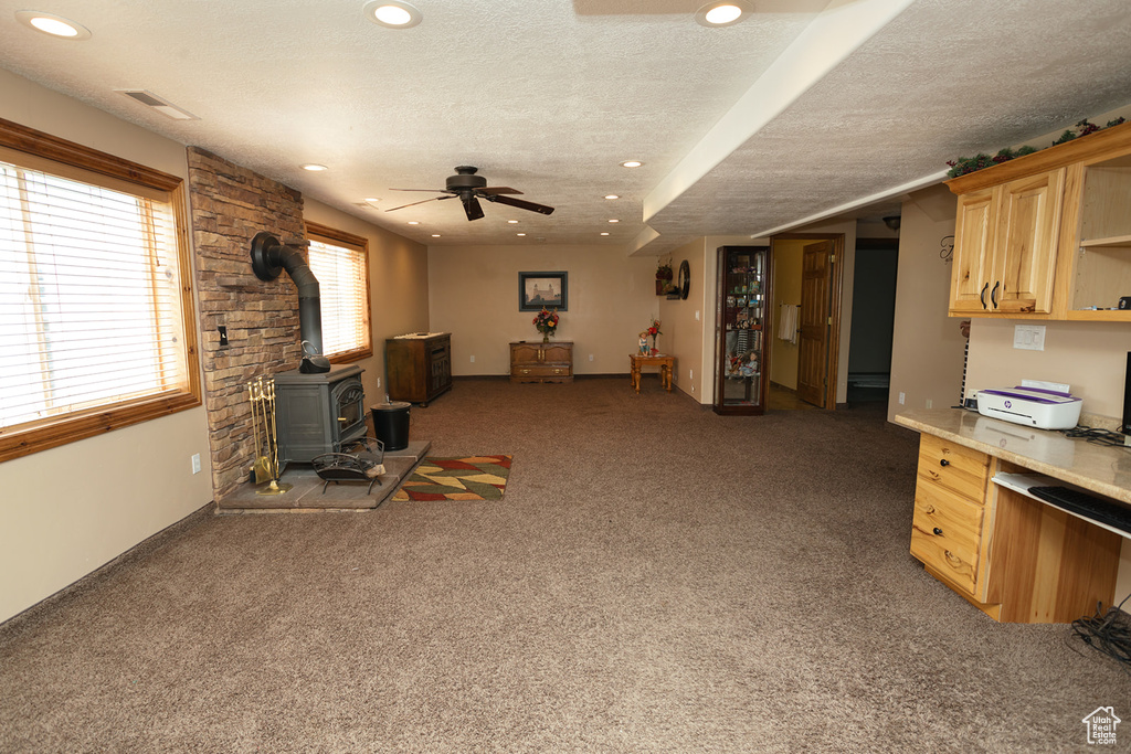 Living room featuring a wood stove, carpet, a textured ceiling, and ceiling fan