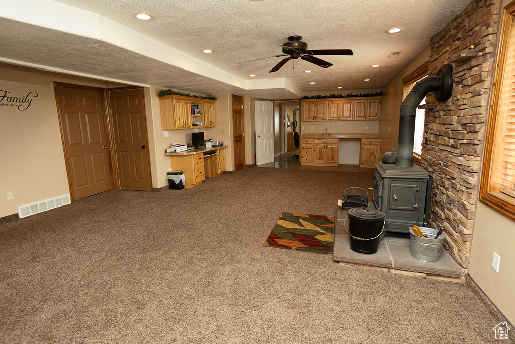 Unfurnished living room featuring a textured ceiling, a wood stove, carpet flooring, and ceiling fan